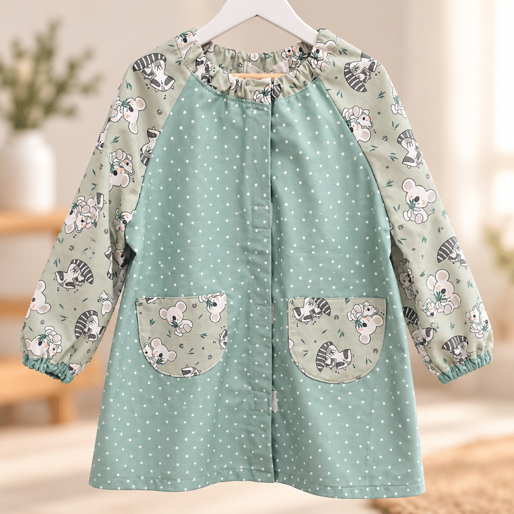 Babi escolar personalizado verde agua con lunares blancos, mangas de koalas y mapaches y dos bolsillos delanteros de The Paradise Noah.